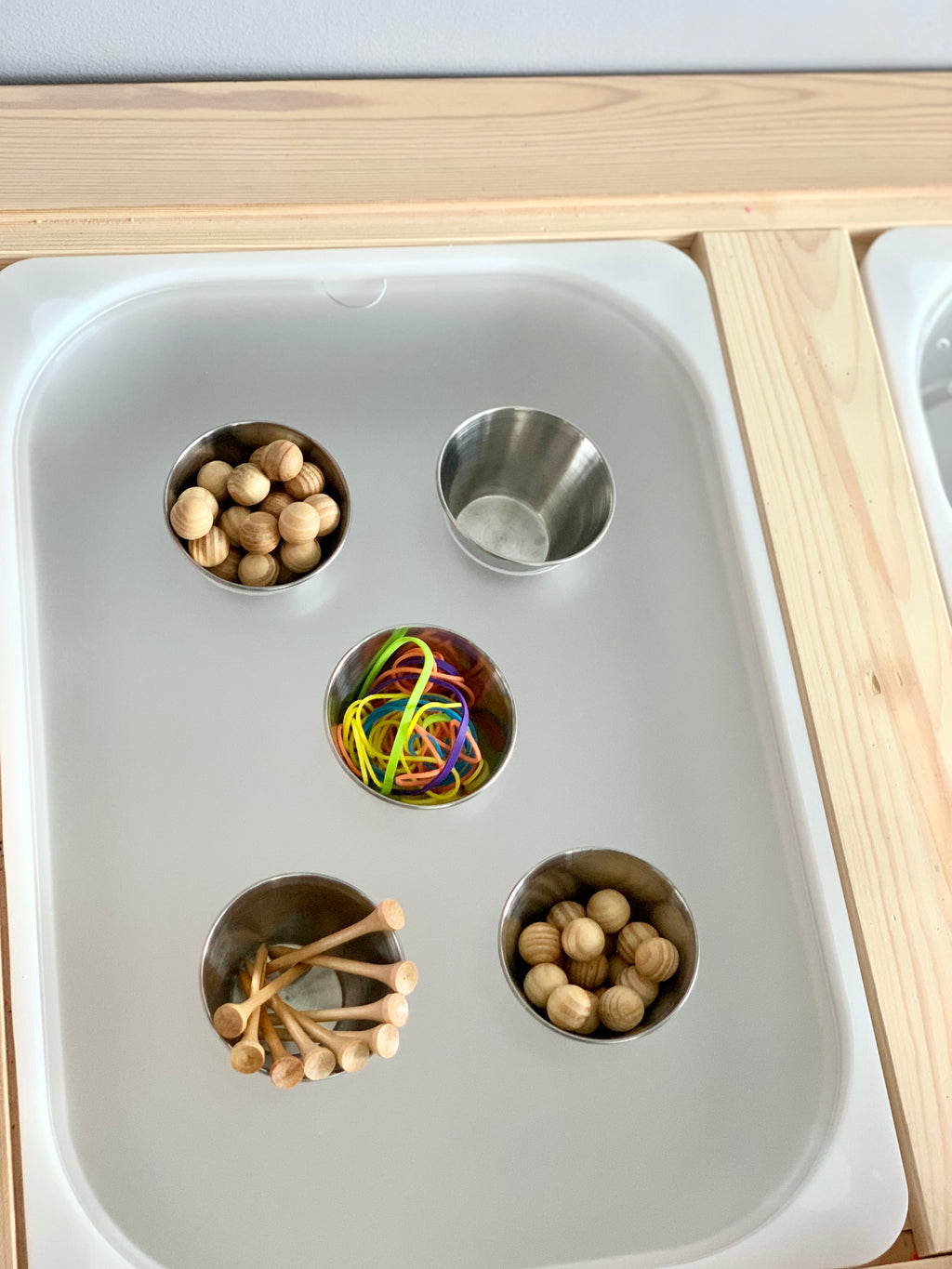 White Flisat tabletop insert with four metal cups holding wooden beads, pegs, and colorful rubber bands in natural wood frame