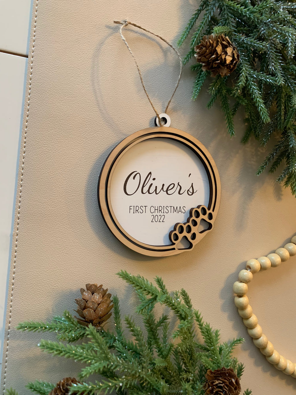 Round wooden Christmas ornament with paw prints and personalized text for a pet's first Christmas 2022