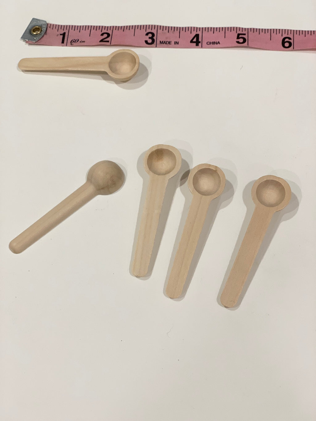 Set of five natural wooden sensory bin scoops with rounded handles placed next to pink measuring tape on white surface