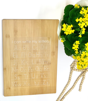 Acrylic dry erase tracing board with uppercase and lowercase letters engraved on natural wood background next to yellow flowers