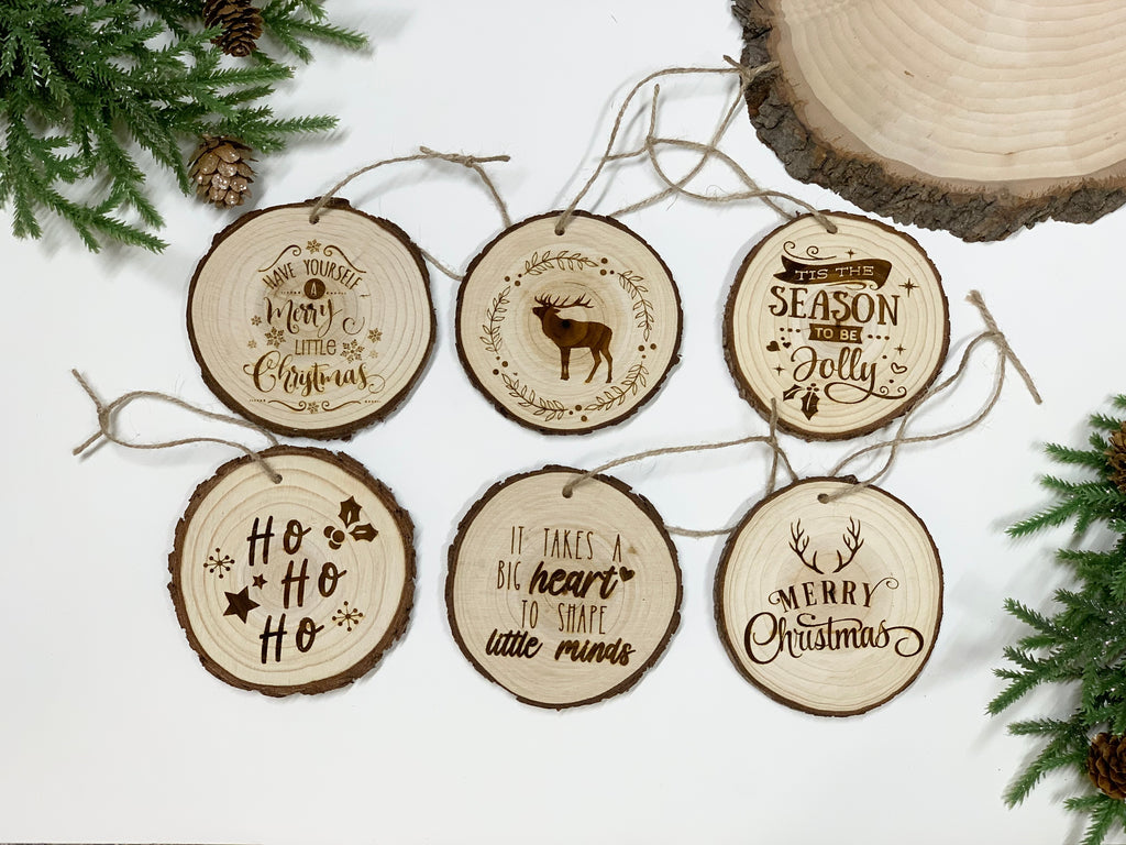 Set of six natural wood Christmas ornaments with burn-engraved holiday sayings and rustic string hangers on white background