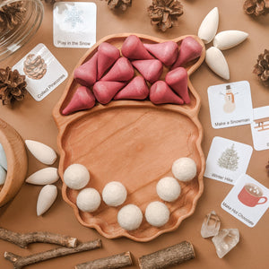 Santa-shaped wooden sensory tray with red and white play pieces and winter-themed activity cards on beige surface