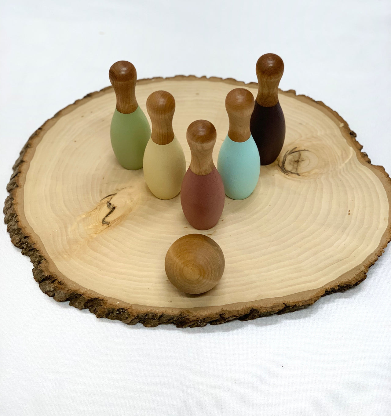 Small wooden five-piece pastel bowling set with ball on natural wood slab background