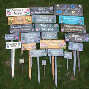 Collection of large personalized wooden garden signs with floral decorations and white cursive lettering on various painted backgrounds