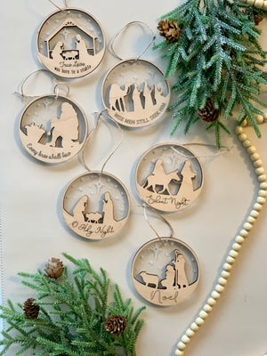 Two-layer wood and acrylic nativity Christmas ornaments with different religious scenes and holiday phrases on white background
