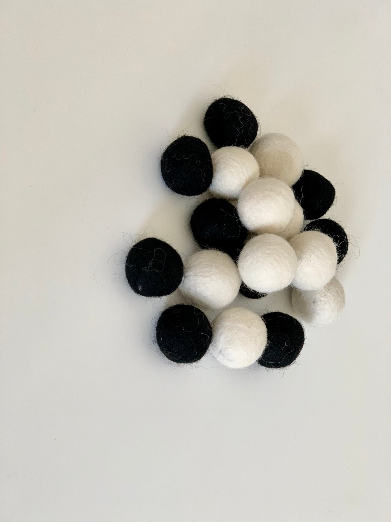 Assortment of black and white felt balls scattered on white background for sensory play or crafts