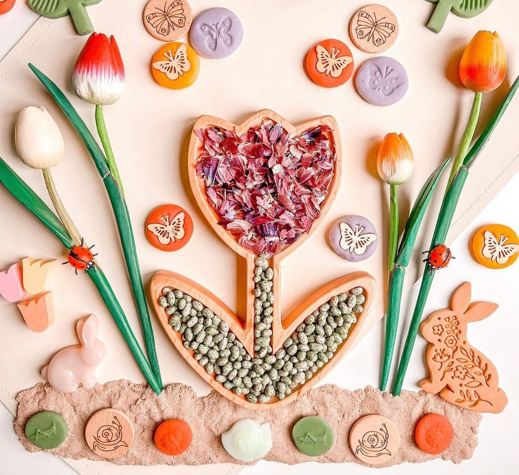 Tulip-shaped sensory tray filled with dried flower petals and seeds surrounded by wooden tulips and nature-themed play items