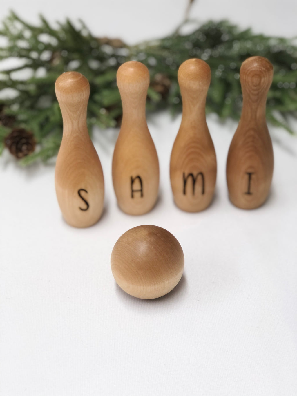 Personalized wooden bowling pins spelling SAMI with a wooden ball, perfect custom toddler toy set on white background.