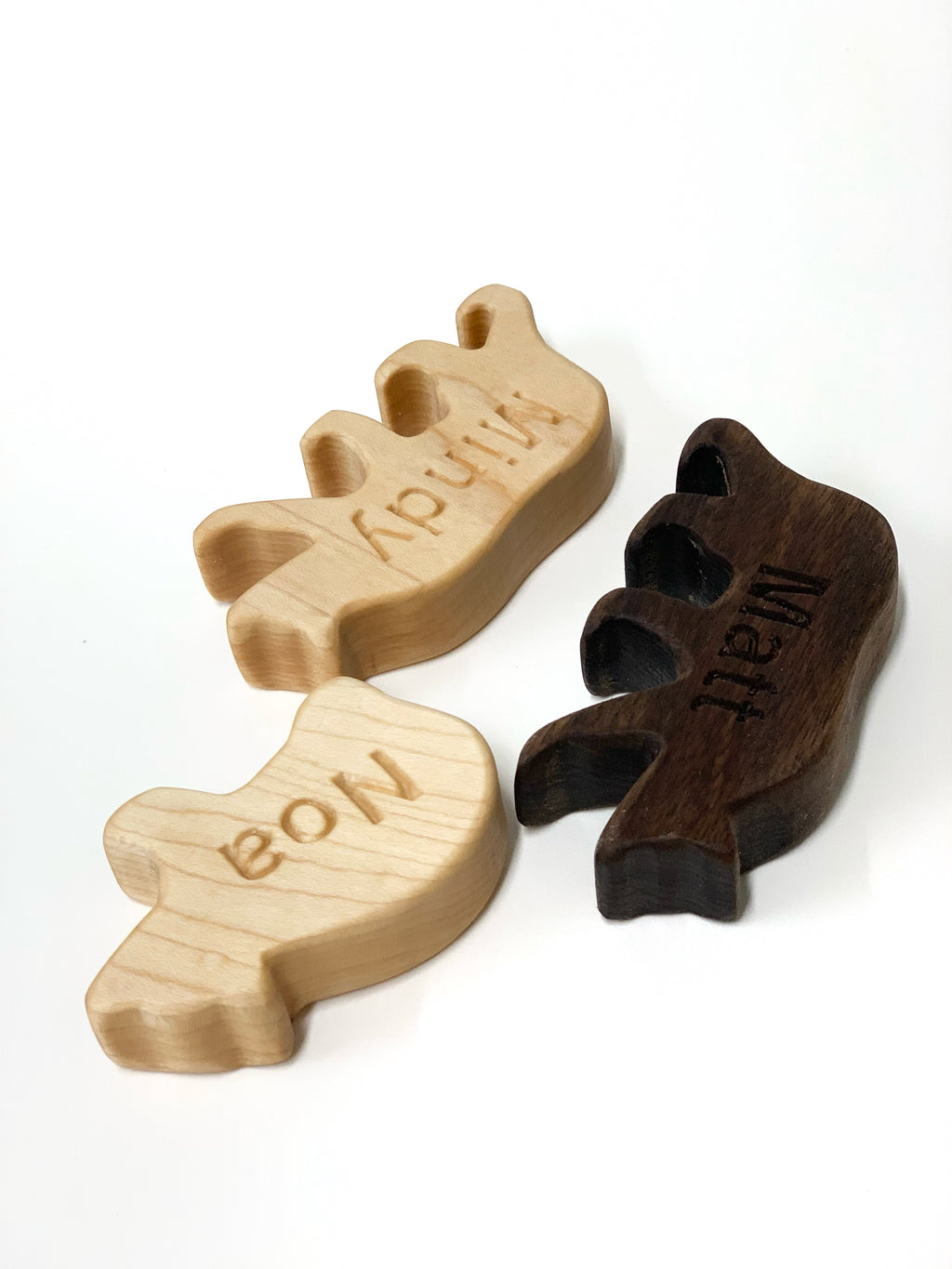 Three wooden animal-shaped pieces with personalized engraved names on light and dark wood surfaces on white background