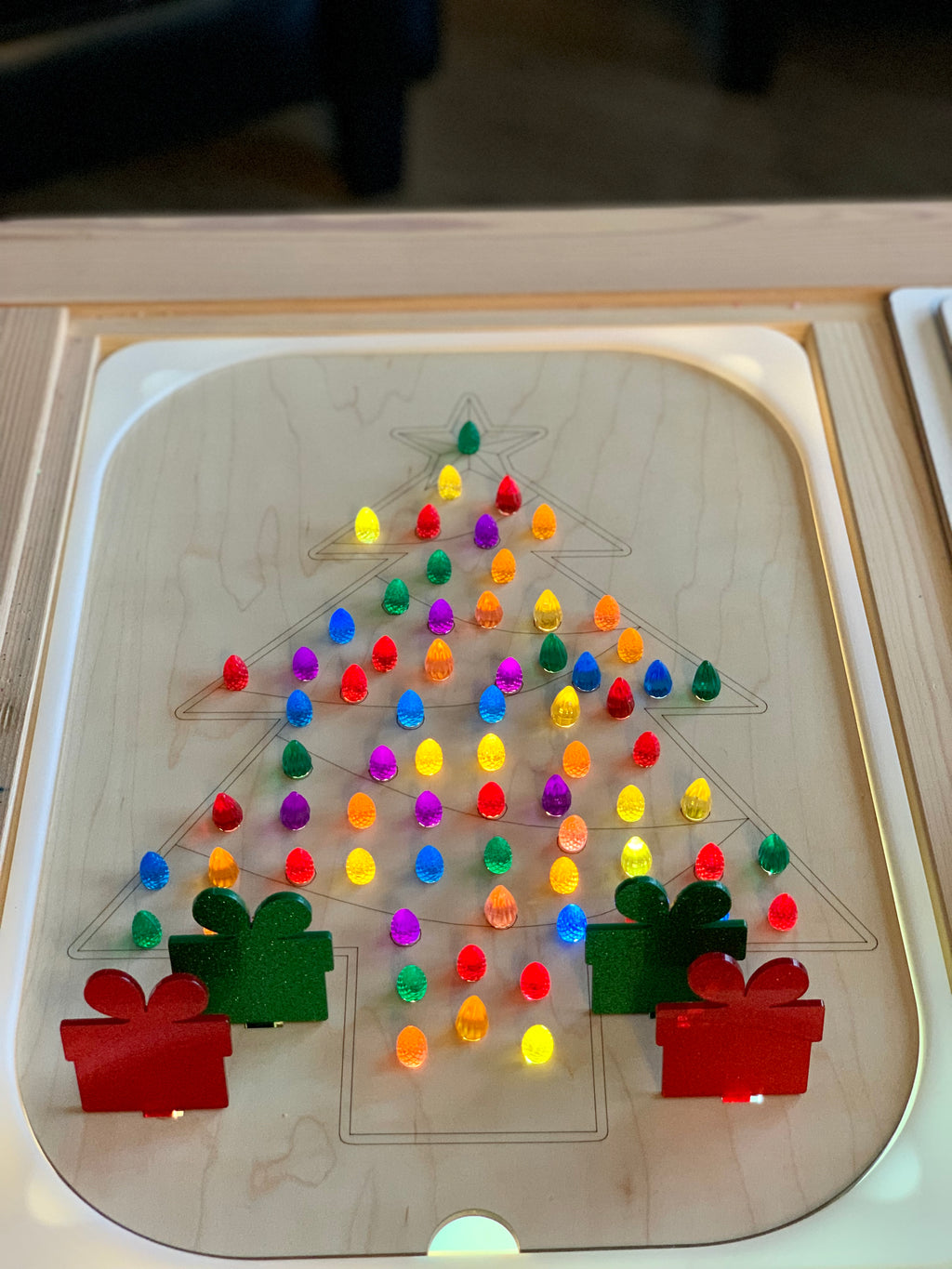 Wooden Christmas tree Flisat insert with colorful light pegs and four acrylic present pegs on light wood surface