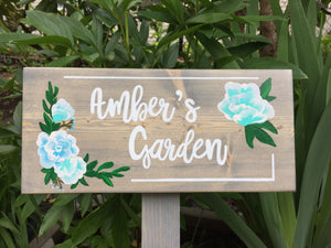 Large personalized wooden garden sign with white cursive letters and blue floral accents on natural wood background