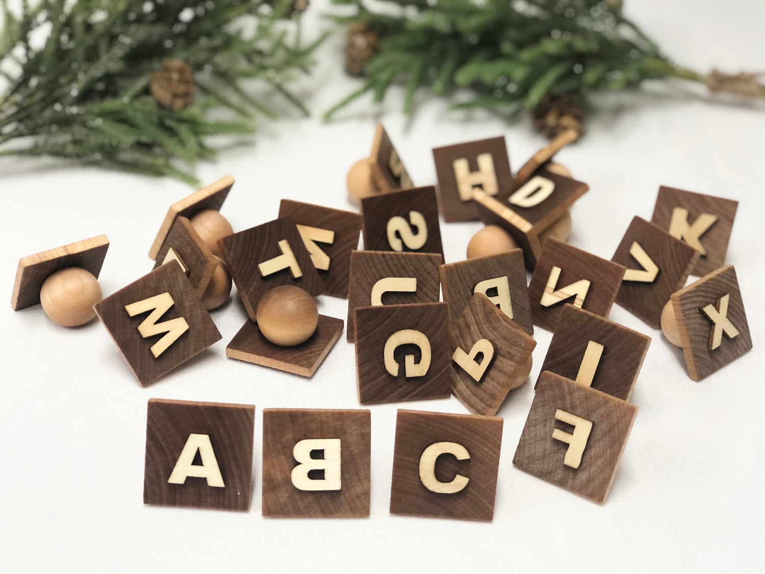 Wooden alphabet play dough stampers with engraved capital letters scattered on white surface with green foliage background