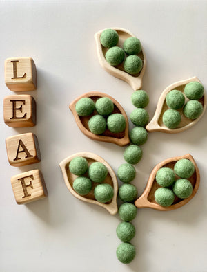 Small wooden leaf-shaped sensory trays filled with green felt balls arranged with wooden letter blocks spelling leaf on white surface