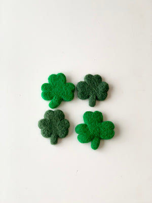 Four handmade felt clovers in varying green shades arranged on a white background