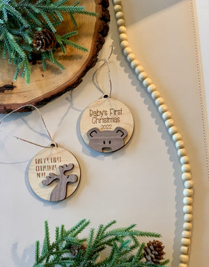 Two wooden Baby’s First Christmas 2021 and 2022 ornaments with moose and bear designs on white surface