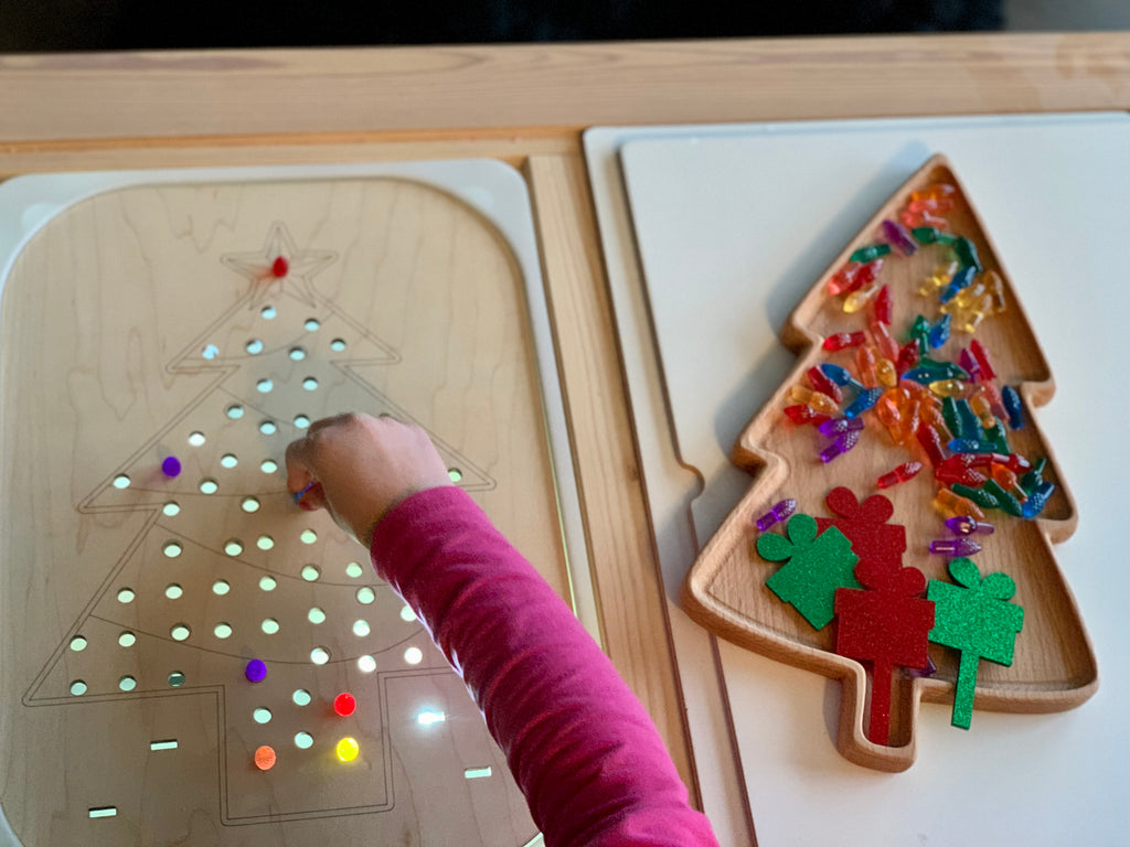 Child placing colorful pegs into light-up wooden Christmas tree Flisat insert with acrylic present pegs on table
