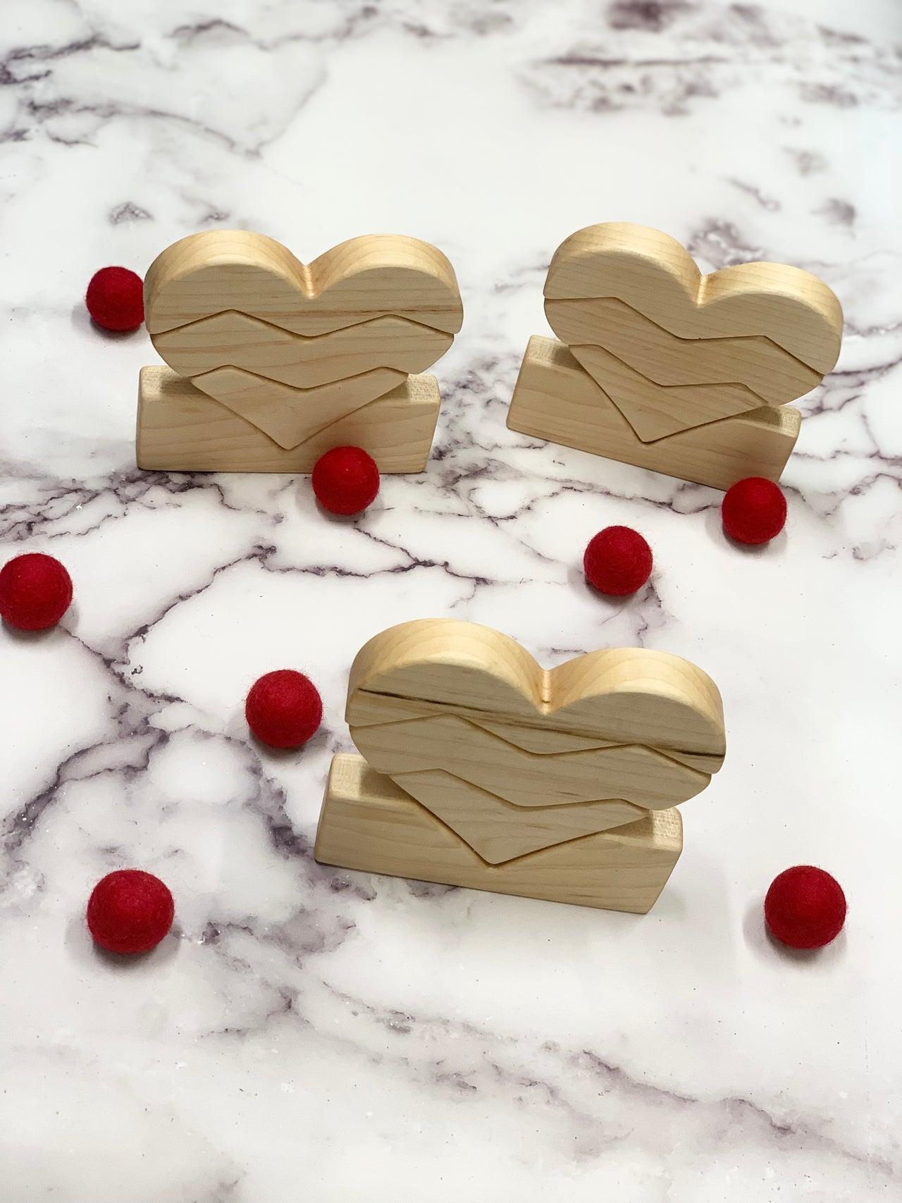 Natural wooden heart stacking toys arranged on marble surface with scattered small red felt balls