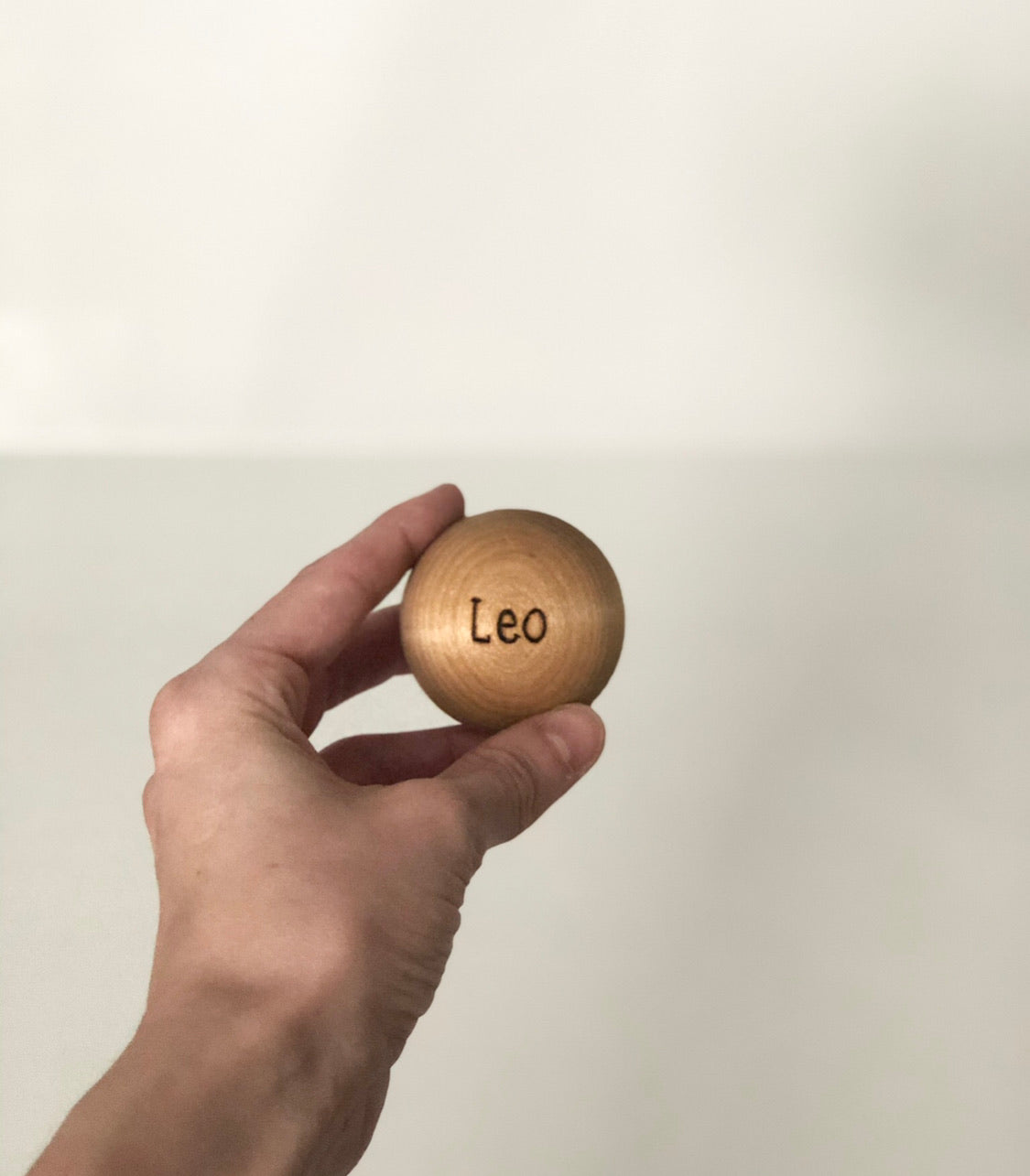 Hand holding a small wooden ball engraved with the name Leo, extra ball for bowling set accessory