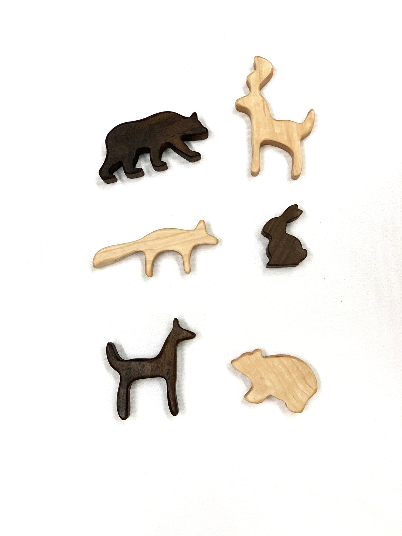 Set of six natural and dark wooden animal toy figurines including deer, bear, rabbit, fox, and wolf on white background