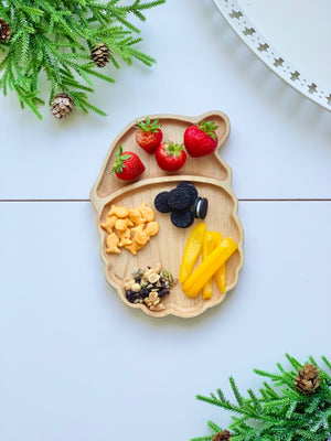 Santa-shaped wooden sensory tray with strawberries, yellow pepper strips, cookies, trail mix, and goldfish crackers on white surface