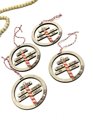 Round wooden Christmas ornaments with personalized family names on red and white striped North Pole signs on white background