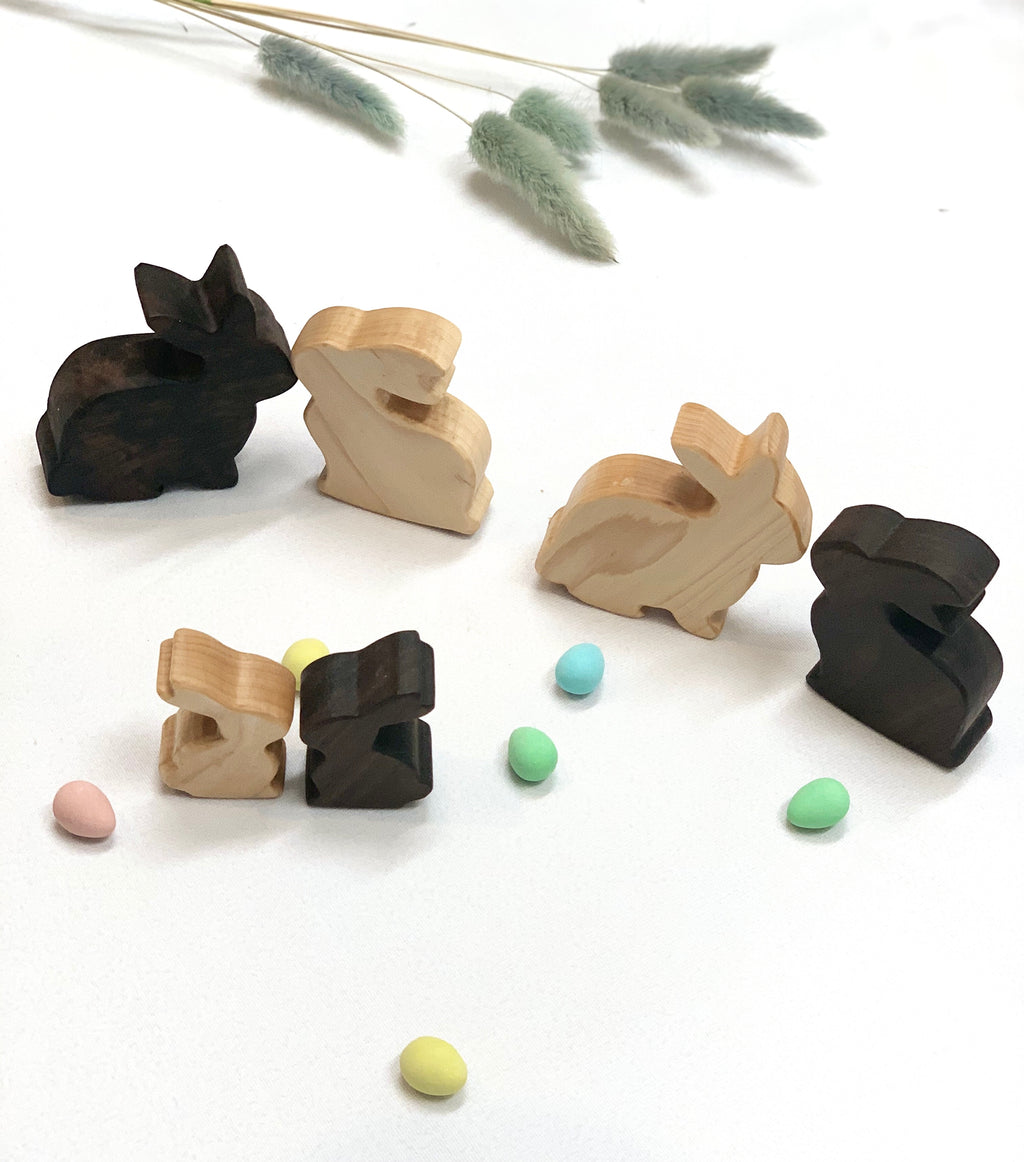 Set of handcrafted wooden toy bunnies in light and dark wood finishes with pastel colored small eggs on white surface
