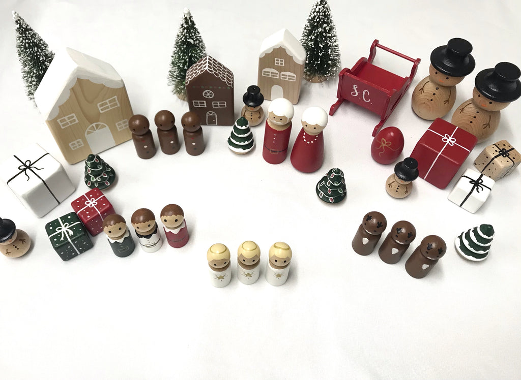 Assorted Christmas peg dolls and miniature wooden houses with trees and wrapped presents on white background