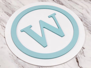 Round 3D monogram wooden sign with light blue letter W and circle on white layered MDF background
