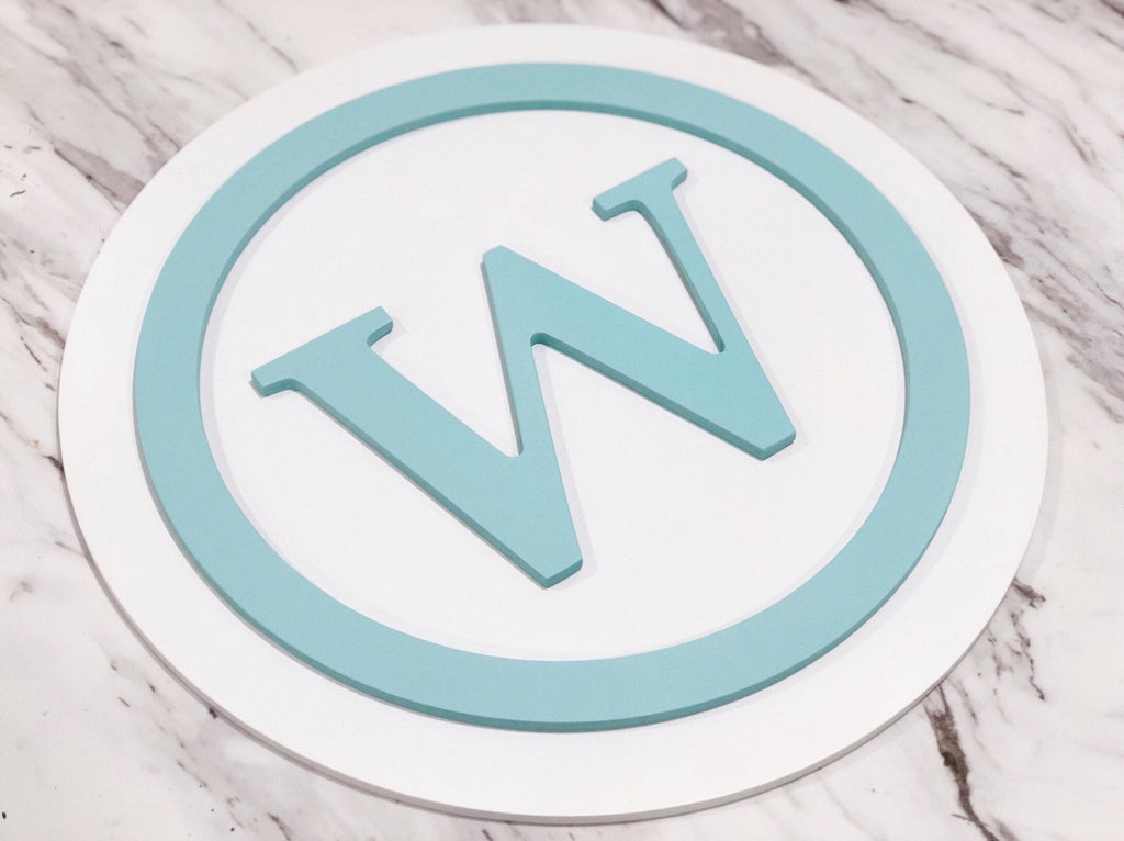 Round 3D monogram wooden sign with light blue letter W and circle on white layered MDF background