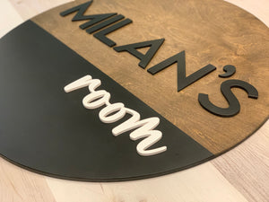 Round half painted wooden 3D name sign with black and brown sections and black and white raised letters on floor