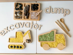 Wooden sensory trays shaped like excavator and dump truck filled with colored rice and natural materials on white surface