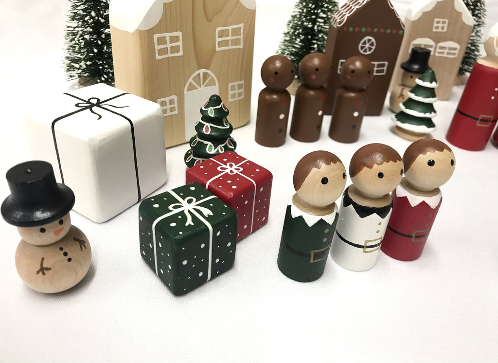 Small painted wooden peg dolls including snowman, elves, presents, trees, and houses on white surface