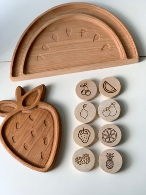 Wooden fruit-shaped trays with engraved seed designs and round wooden memory game discs with fruit illustrations