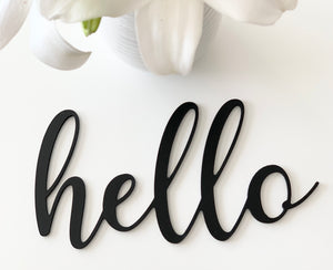 Black cursive custom word cutout spelling "hello" on white background with white flower petals above