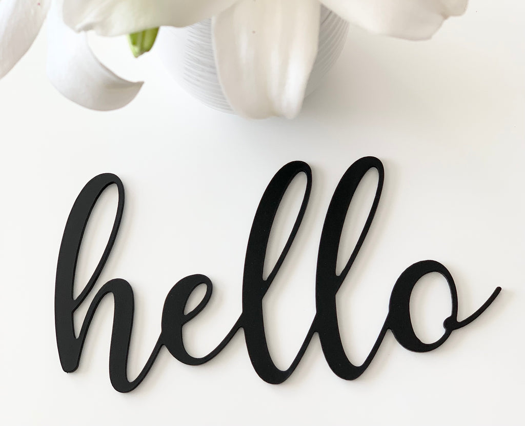 Black cursive custom word cutout spelling "hello" on white background with white flower petals above