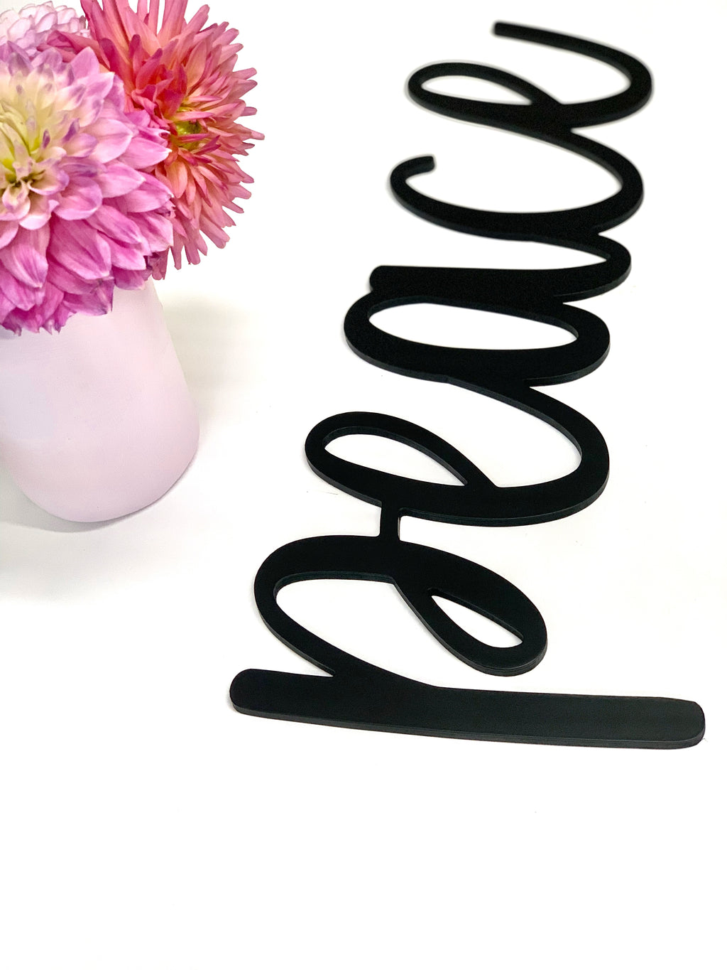 Black custom wooden word cutout with cursive letters displayed next to pink and white flower arrangement in pink vase
