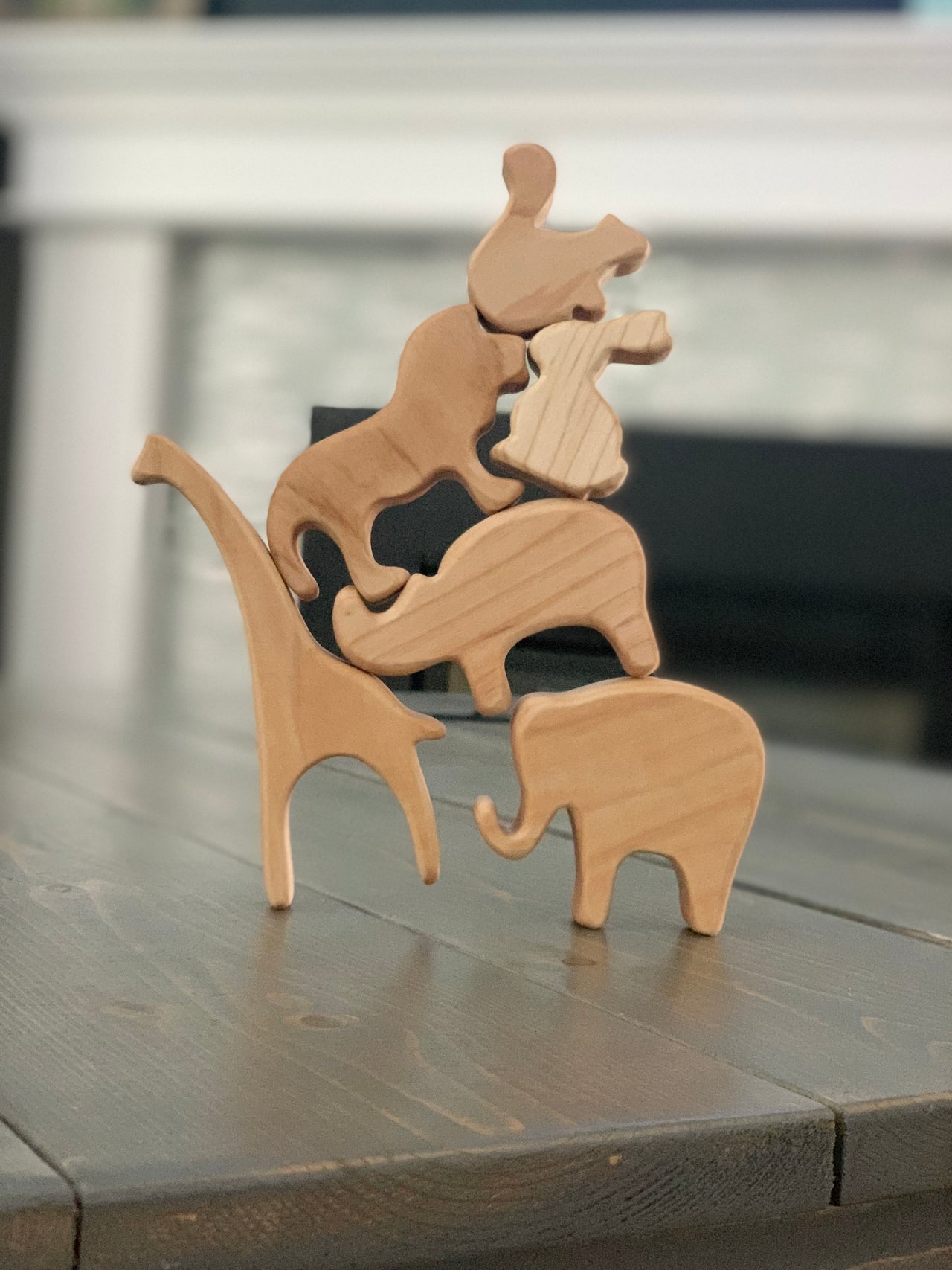 Stacked natural wooden animal toy figurines including elephant, giraffe, and others on wooden table surface