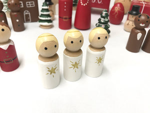 Three small wooden peg dolls painted as angels with white bodies and gold star decorations on white background