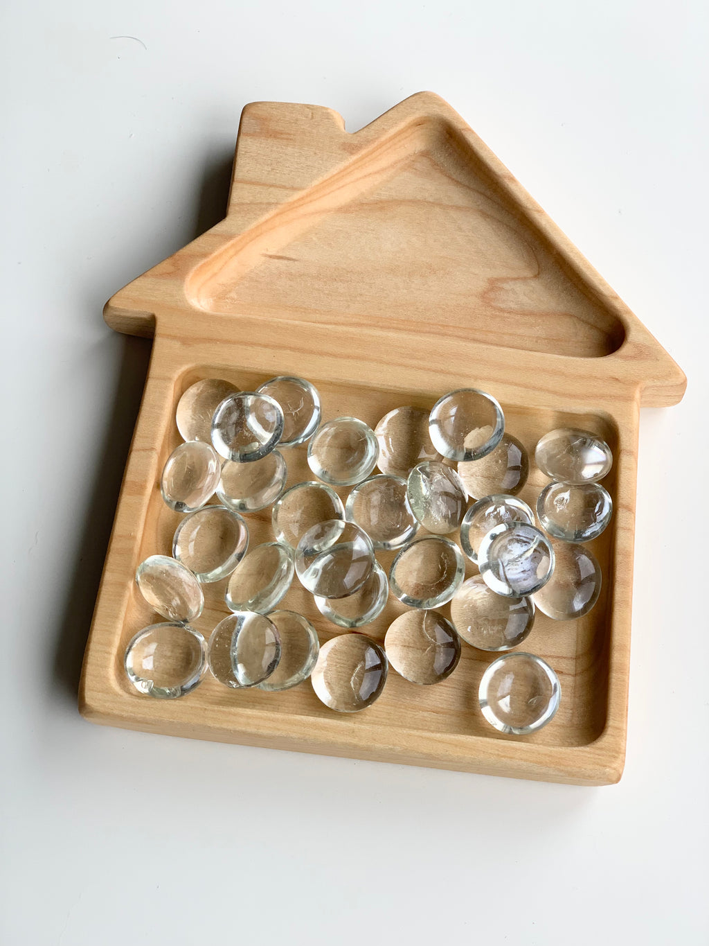 Small clear glass treasure gems arranged on natural wood tray shaped like a house on white background