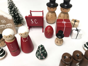 Hand-painted wooden Christmas peg dolls including Santa, Mrs Claus, snowmen, reindeer, presents, trees, and holiday accessories on white background