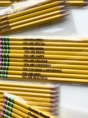 Set of 10 yellow affirmation pencils with inspirational black text and pink erasers arranged on white background