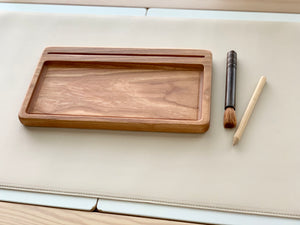 Rectangular wooden sensory tray with natural wood grain, and two wooden stylus tools on beige surface