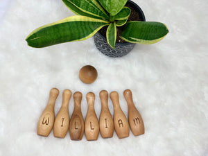 Personalized wooden bowling set with name William, including pins and ball, displayed on white fur next to green plant in pot