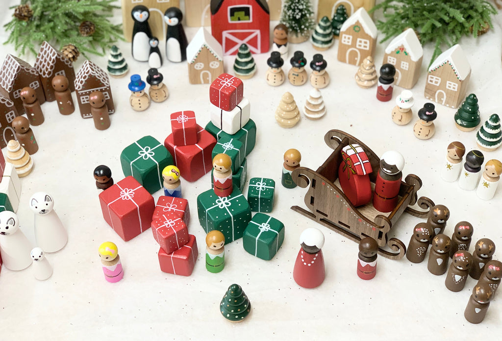 Assorted hand-painted Christmas peg dolls with presents, trees, snowmen, houses, reindeer, and sleigh on white background