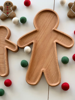 Large wooden person-shaped plate or sensory tray surrounded by colorful felt balls and gingerbread decorations
