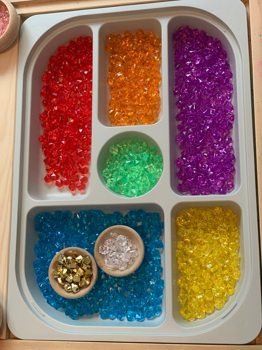 White Flisat sorting tray filled with colorful translucent gems and two small wooden bowls on wooden table