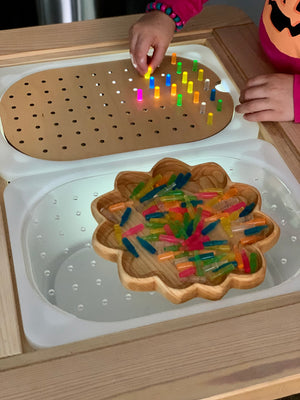 Child placing colorful plastic pegs into small hole geometric light board on wooden Flisat tabletop insert