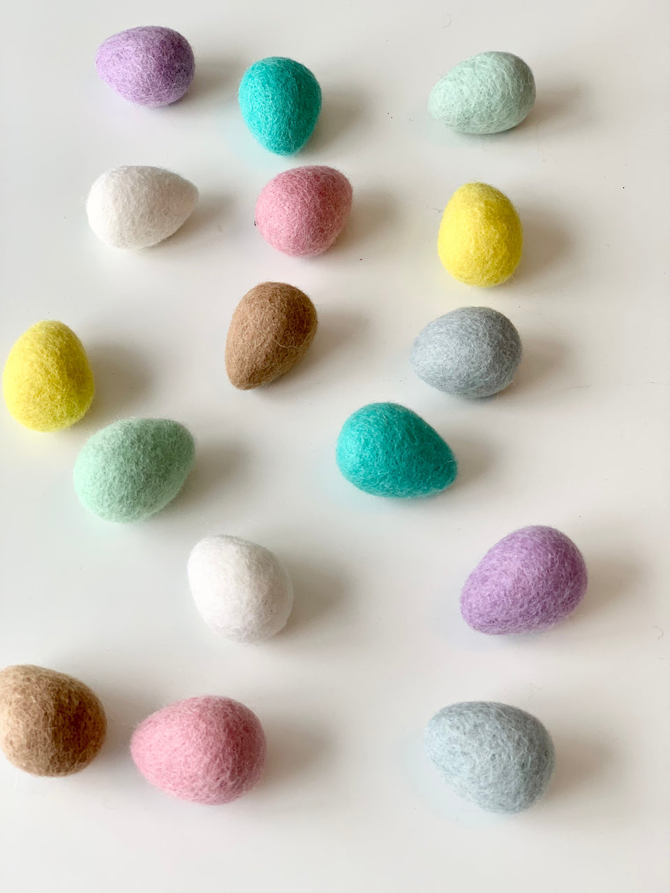 Assorted pastel-colored felt Easter eggs made from 100% wool arranged on white surface