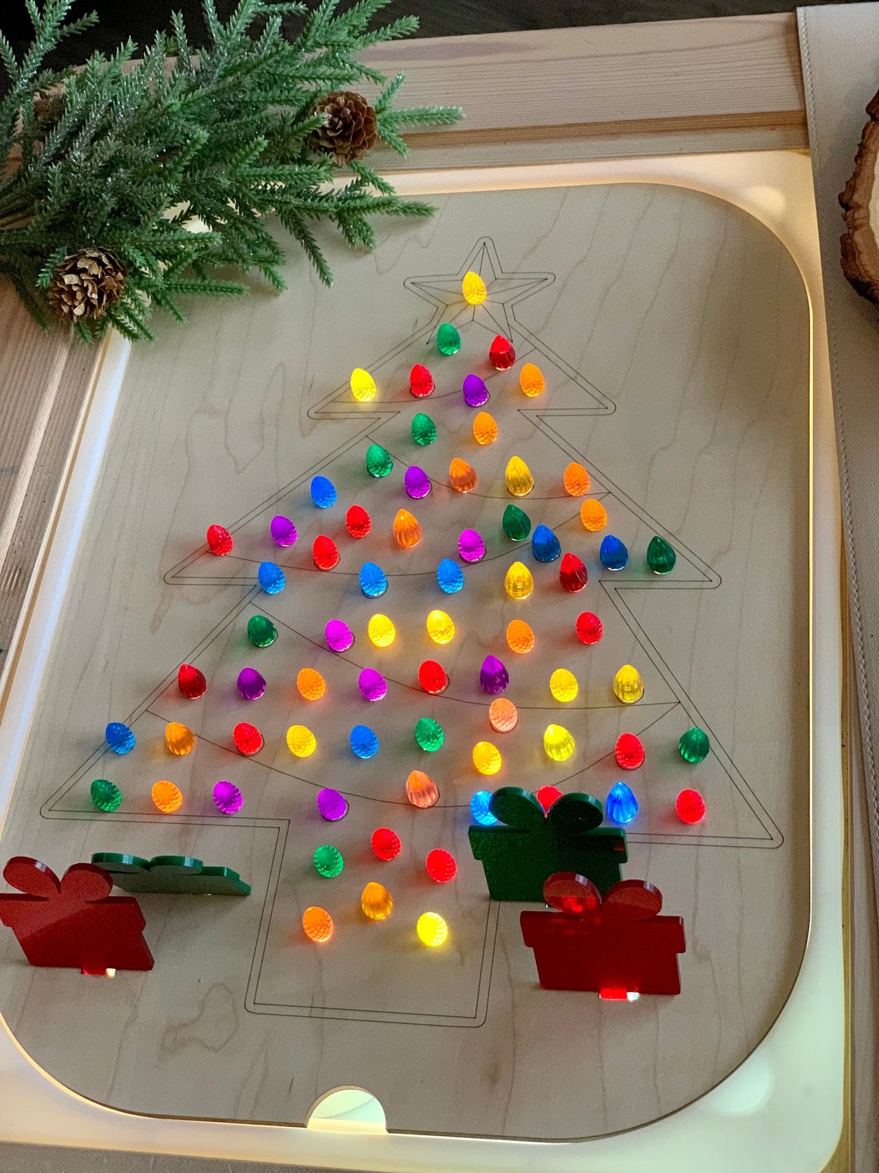 Wooden Christmas tree geometric board insert with colorful light-up pegs and wooden gift shapes on light wood table