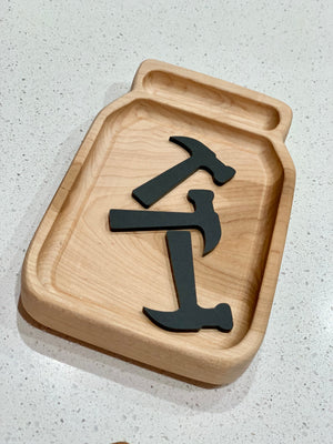 Wooden jar-shaped tray holding three black acrylic loose parts shaped like hammers on light countertop